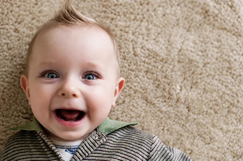 A laughing baby lying on a beige carpet